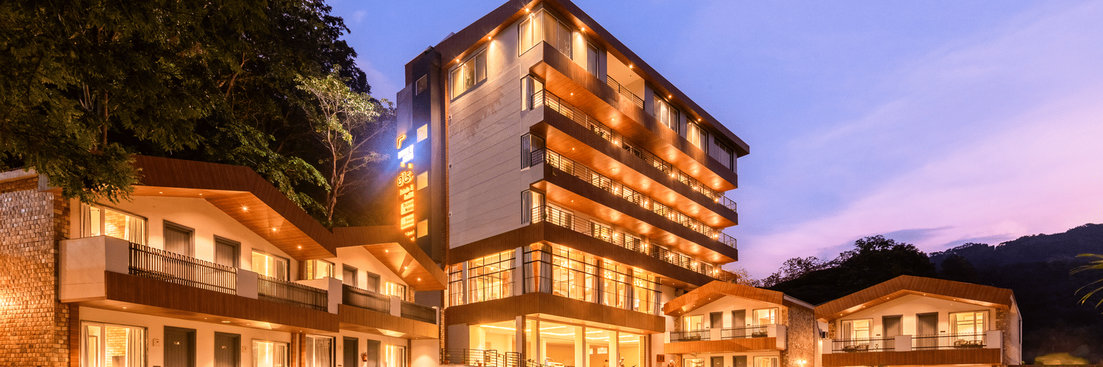 Exterior facade view of DLS Divine River Resort and Spa with warm lighting and garden area taken in the evening 